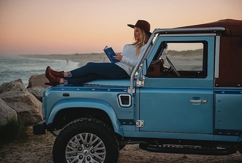 Woman reading on blue Defender at beach