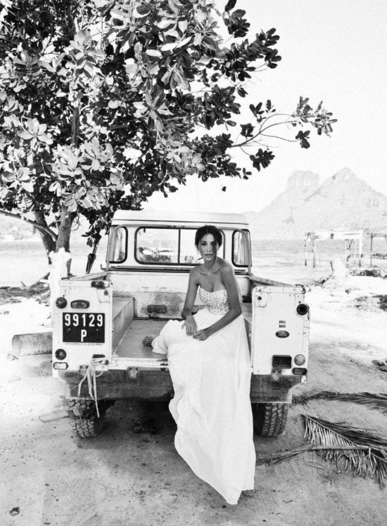 Woman in white dress in vintage Land Rover pickup at beach