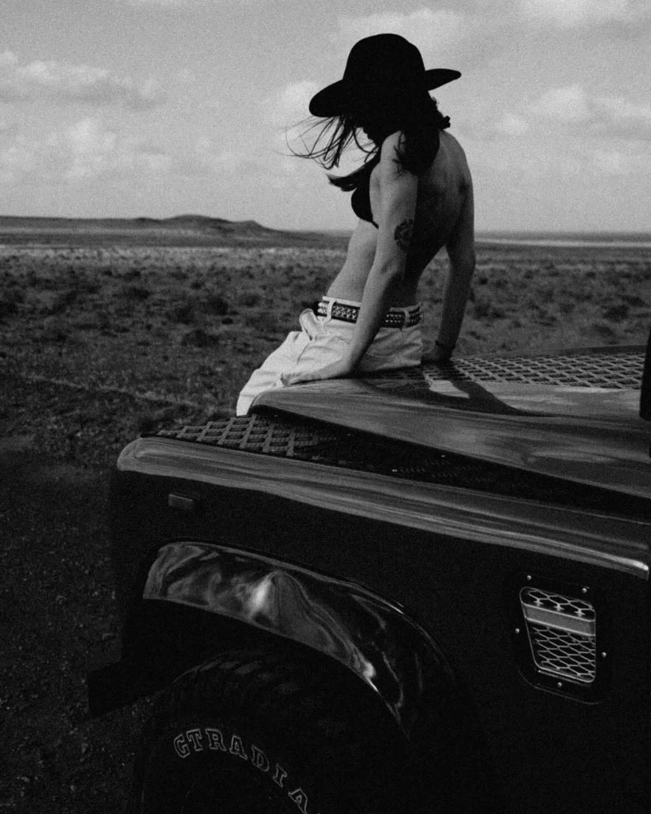 Black and white — woman on Defender hood in desert