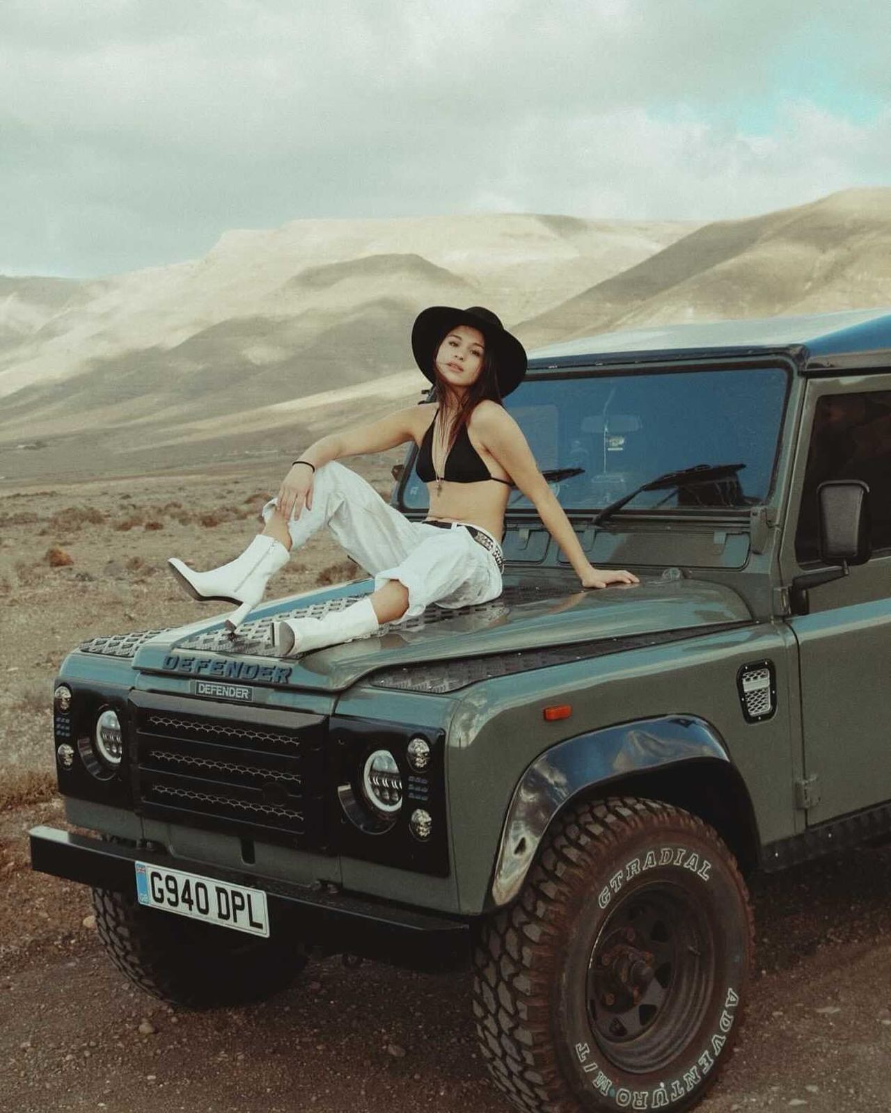 Woman on olive green Defender hood in arid mountains