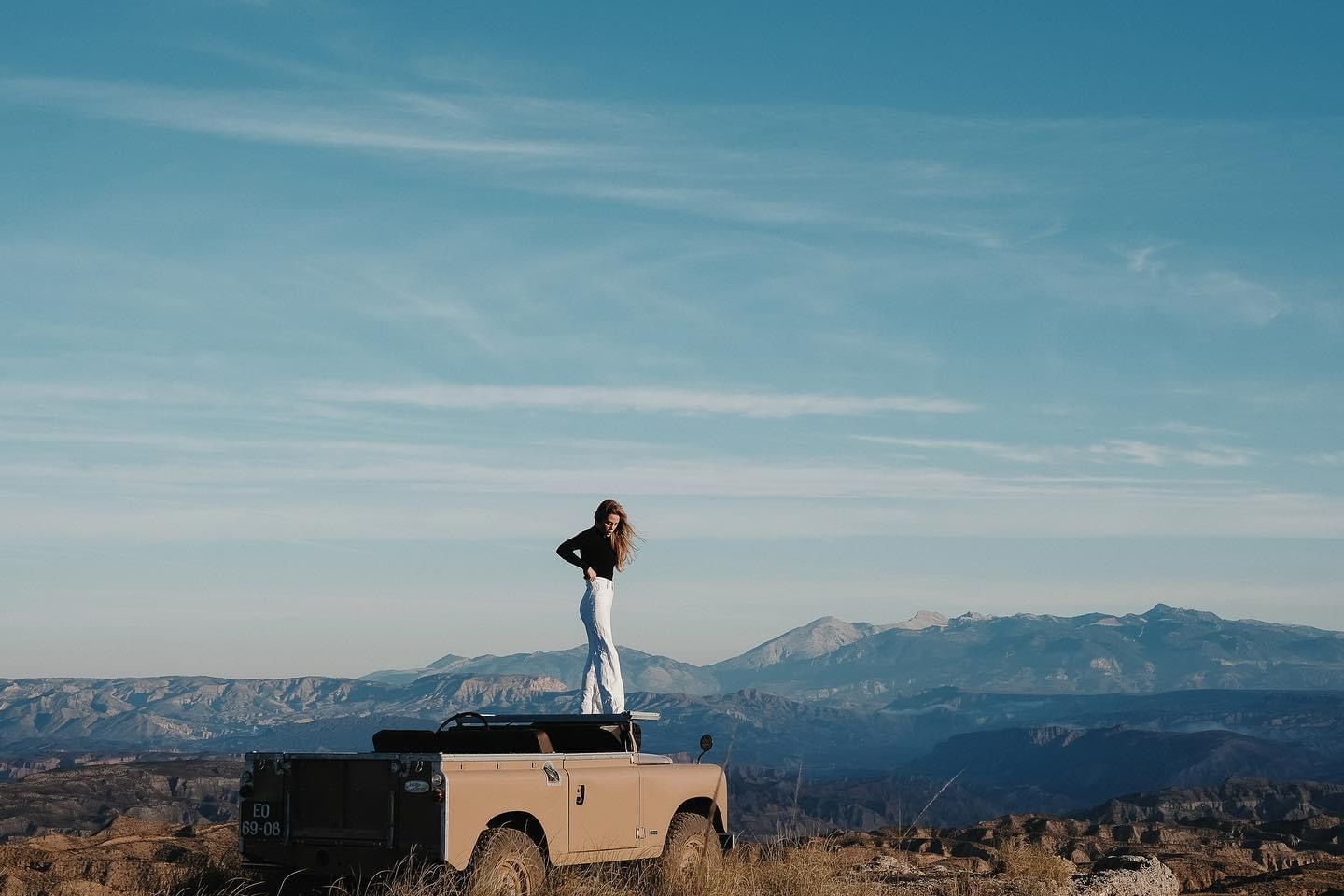 Woman standing on tan Defender soft top in mountain vista