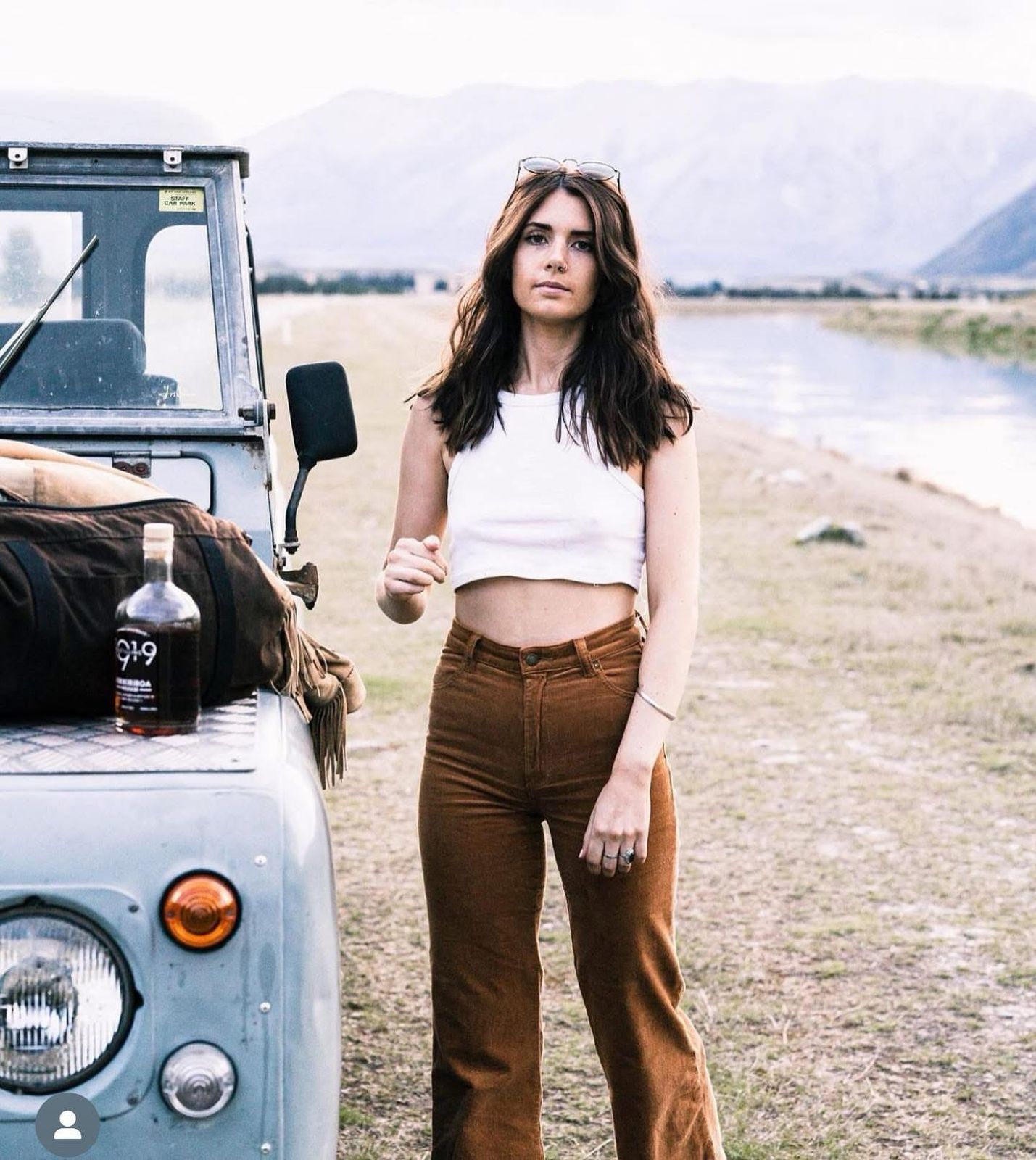 Light blue Defender with duffel by river and mountains